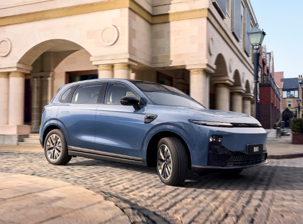 Blue SUV driving on a cobblestone street by a building with arches.