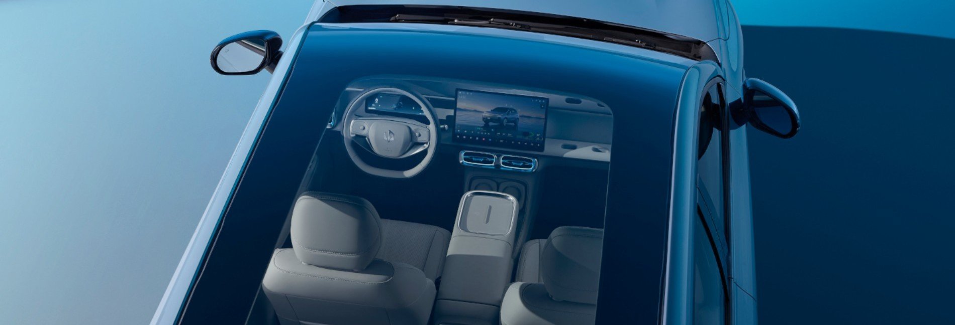 Overhead view of car interior through glass roof, showing steering wheel and digital display.